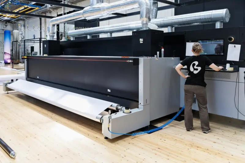Nainen seisoo suuren printterin vieressä.