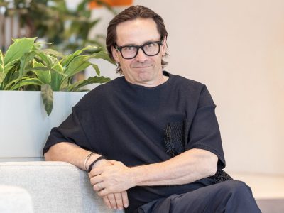 Lasipäinen mies istuu ja hymyilee