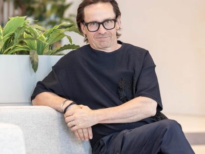 Lasipäinen mies istuu ja hymyilee